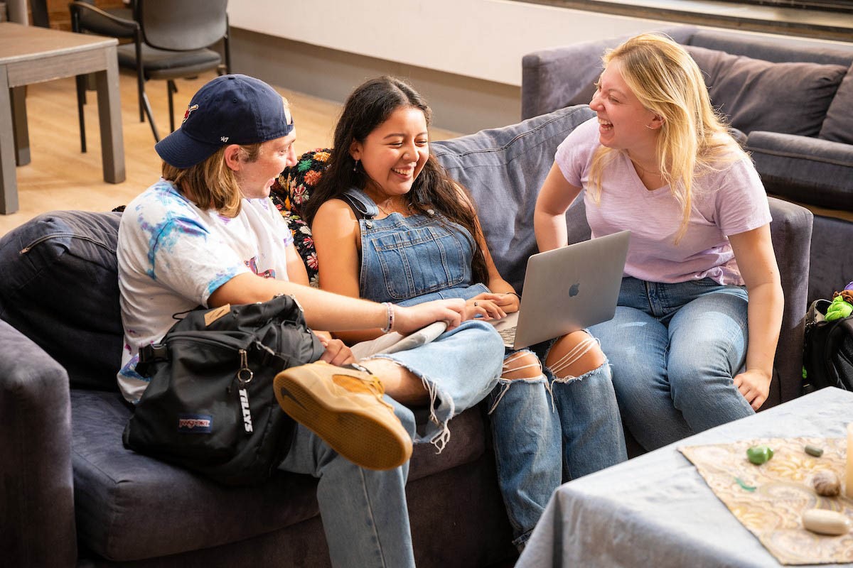 Students looking at a computer on a couch while laughing