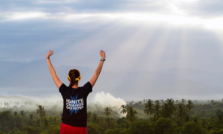 Female student in Villanova shirt raises arms above head as she looks over landscape of Peru.