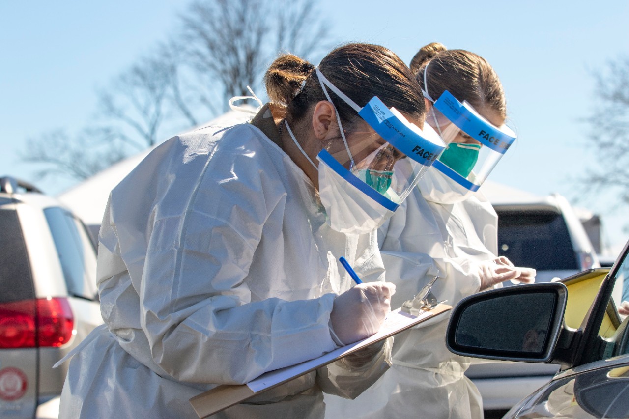Two female nurses write on clip boards while dressed in PPE.