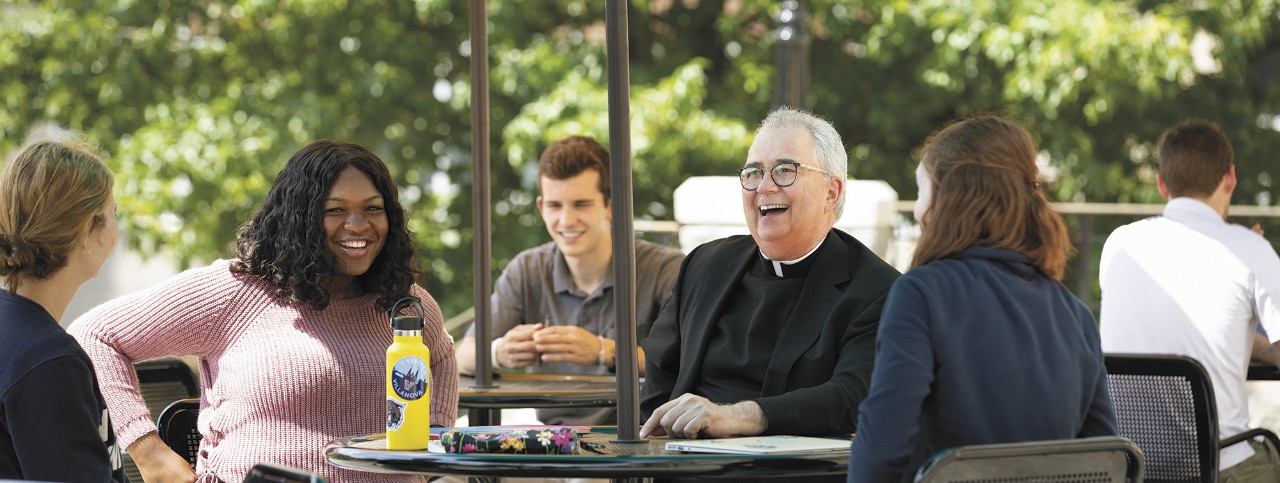 Father Peter seated outside laughing with students