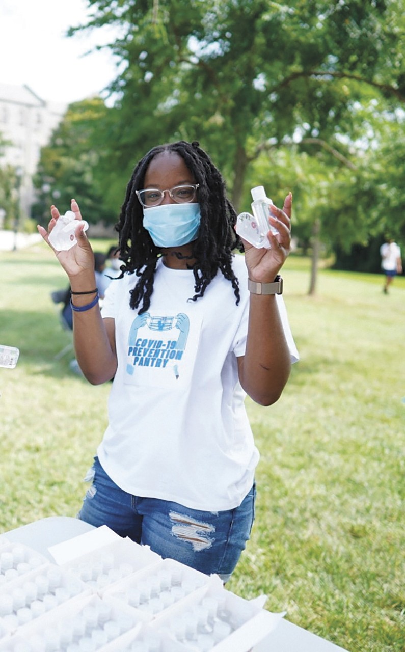 Jasmine Mays outside wearing a mask and holding COVID prevention kits