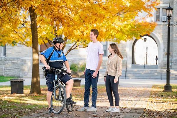 A public safety officer on a bike stops to speak to a male and female student.