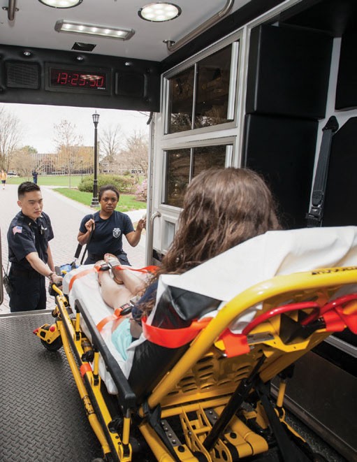 Two emergency response workers help someone in an ambulance