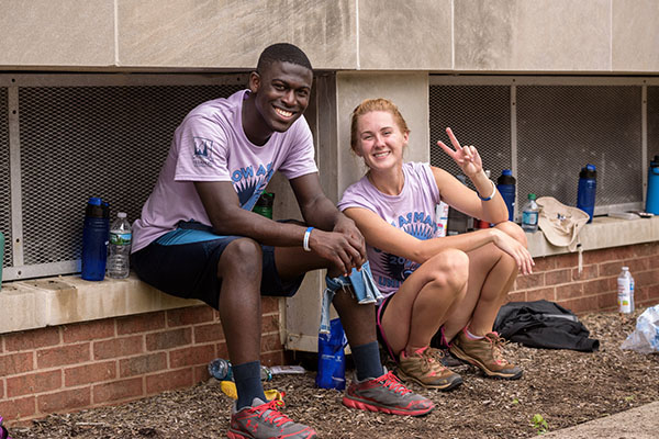 Two smiling students sit together with one holding her finger up in a Villanova "V".