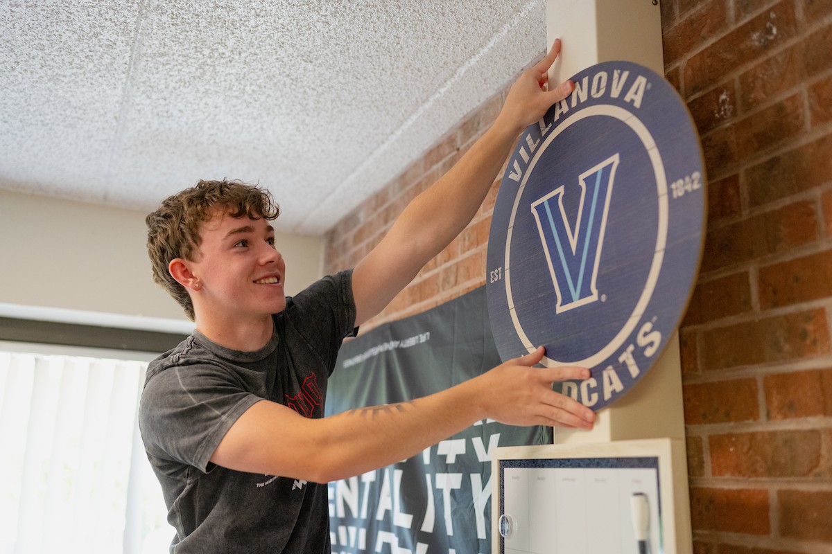 A student hangs a Villanova sign in his residence hall room