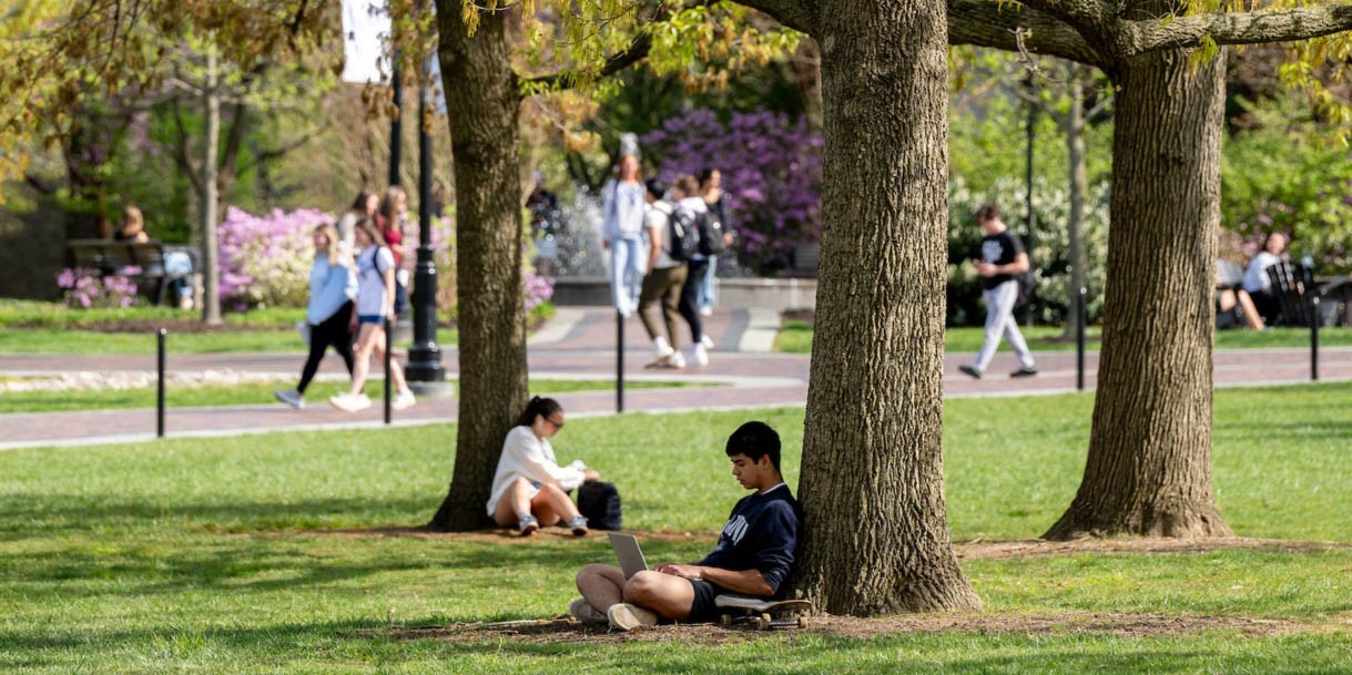 Student working while leaned against a tree on Villanova's campus.