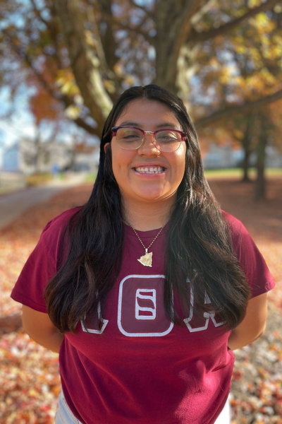 Luz Escobar, smiling, stands in front of a tree in the fall season