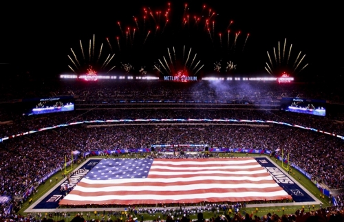 large USA flag stretched across field of Giants Metlife Stadium with fireworks set off in background
