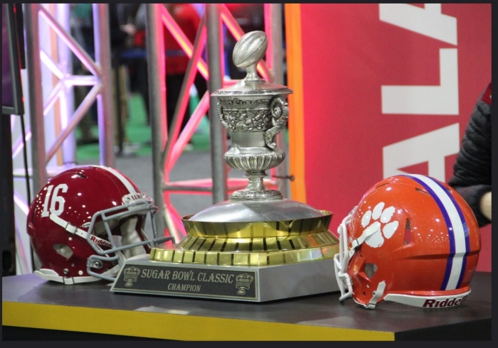 Silver football trophy flanked on either side by football helmets. One red, one orange.