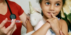 young girl reciving shot holding her unicorn stuffed animal