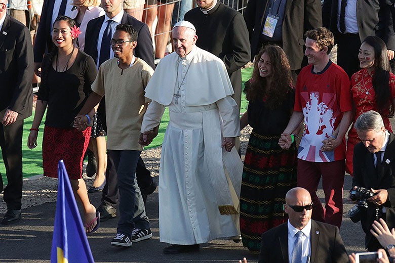 Pope Francis walking in front of crowd, holding hands with teens