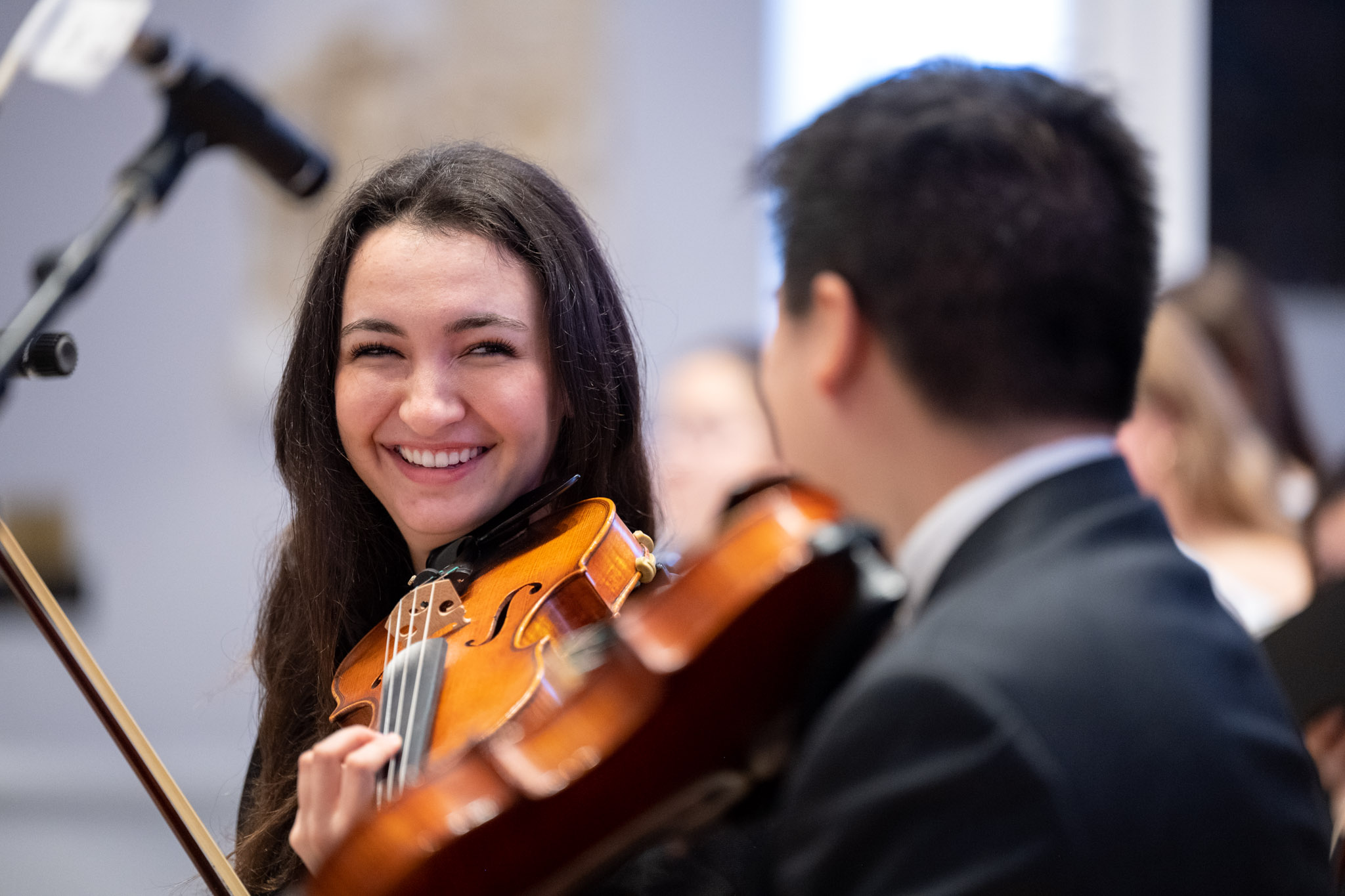 A student holding her violin smiles at a fellow musician