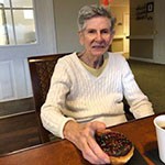 older woman sitting at table holding a pastry
