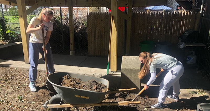 Students digging and shoveling dirt into wheelbarrow 