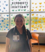 Female nurse stands before a window with colorful hearts.