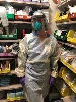 Female nurse dressed in PPE stands in a medical supply closet.
