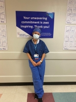 Female nurse leans against a wall in blue scrubs.