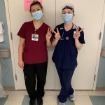 Two female nurses holding their fingers up to make Vs for Villanova.