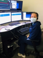 Female nurse sits at a desk reviewing tests with a mask covering her face.