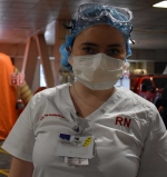 Female nurse dressed in PPE stands in front of an orange tent.