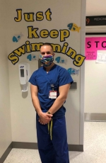 Male nurse dressed in scrubs with a mask covering his mouth and nose.