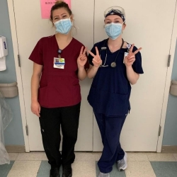 Two femal nurses holding their fingers up to make Vs for Villanova.