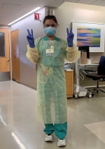 Female nurse dressed in PPE holding her fingers up to form "V"s.