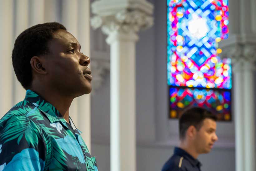 Two men singing in front of a stain glass window