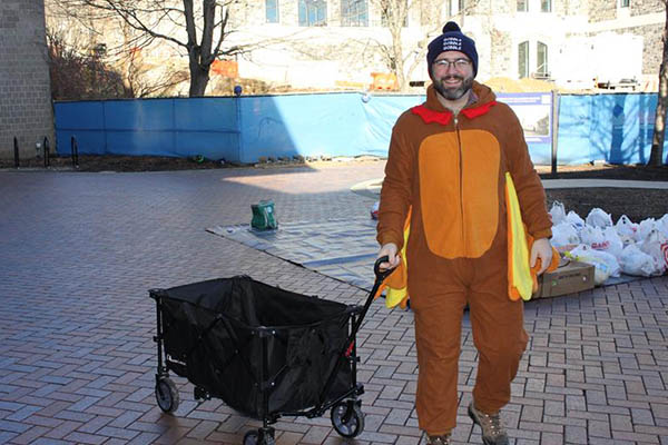Man dressed in turkey oneside pulling food donations in wagon
