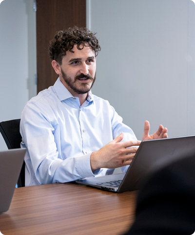 man sitting at a table in front of a laptop and speaking