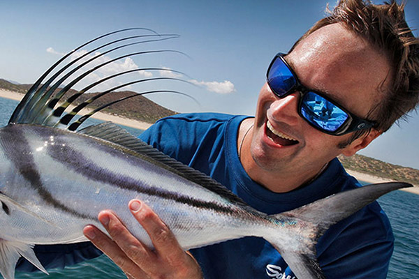 Nick Honachefsky wearing reflective sunglasses and holding a giant silver fish with blue sky and water in the background 