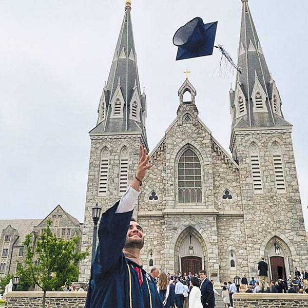 a member of the Class of 2020 tosses his graduation cap in front of St. Thomas of Villanova Church