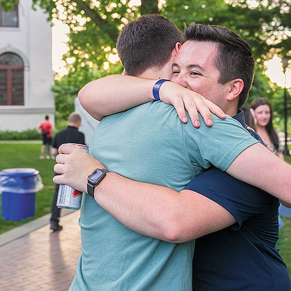 two young male alumni share a hug