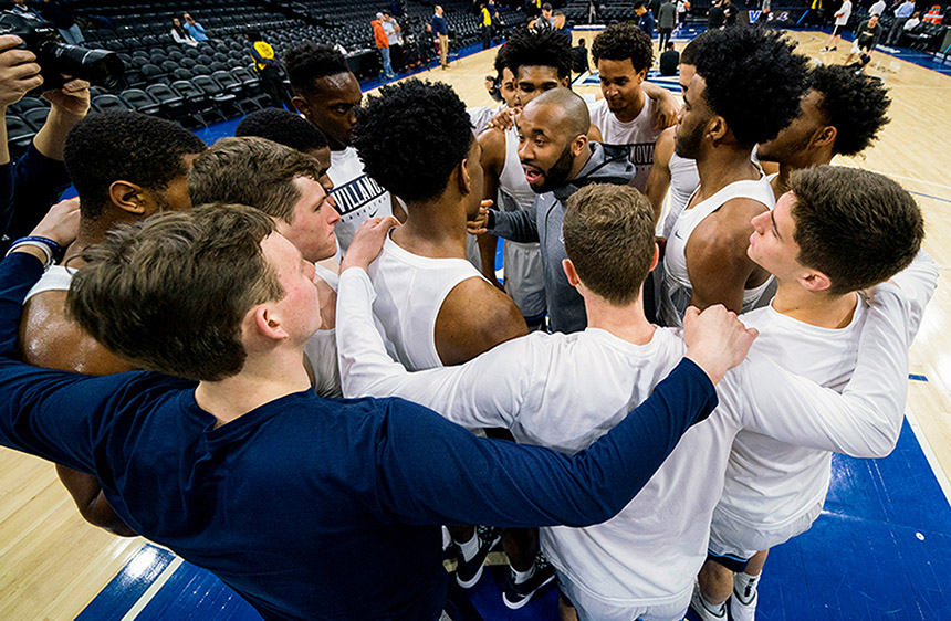 Assistant Coach Kyle Neptune is at the center of a huddle with the Men's Basketball Team