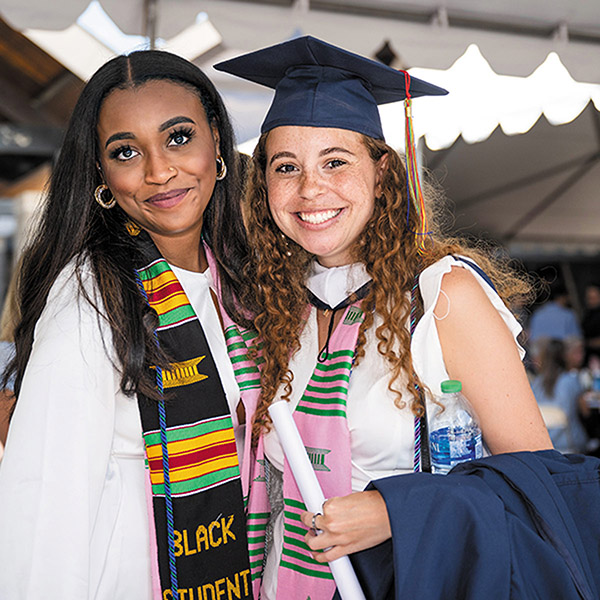 two smiling women dressed in graduation attire stand close together for a photo