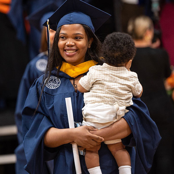 a female Villanova graduate in her cap and gown holds a baby