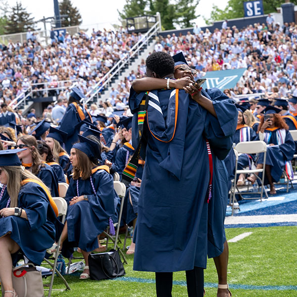 two graduates embrace amidst the crowd in Villanova Stadium during Commencement 