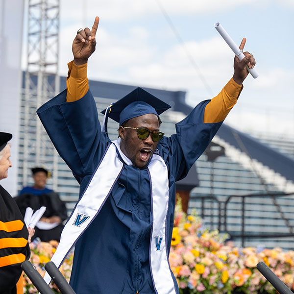 a male Villanova graduate raises his arms in triumph after receiving his diploma