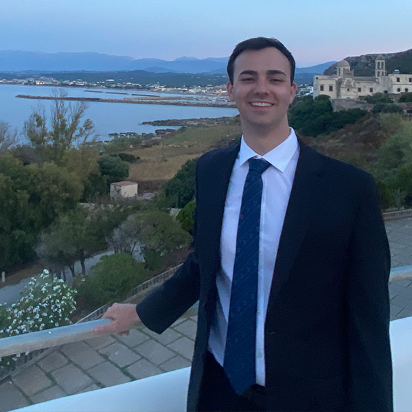 a Villanova student wearing a dark-colored suit poses in front of beautiful scenery