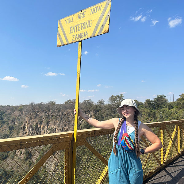 a woman in overalls poses on a yellow bridge in Zambia