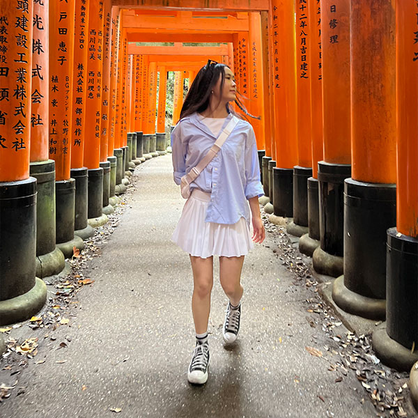 a female student walks through red torii gates in Kyoto, Japan