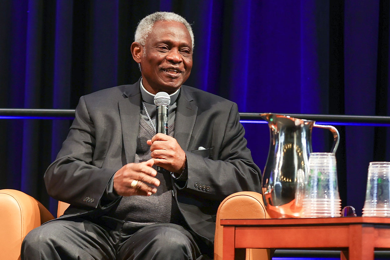 Cardinal Peter Turkson seated in a leather chair and holding a microphone