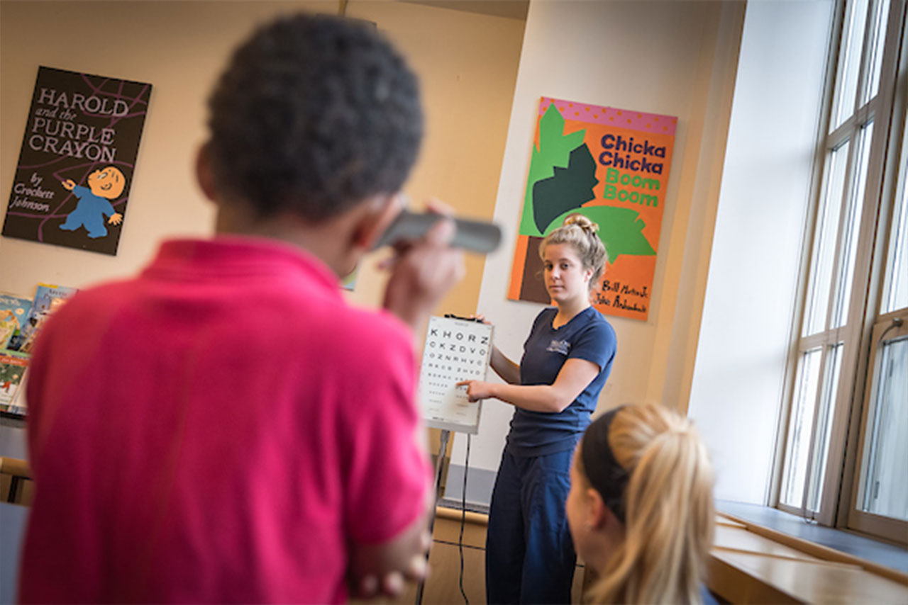 a Villanova Nursing student points at an eye chart being read by a young child