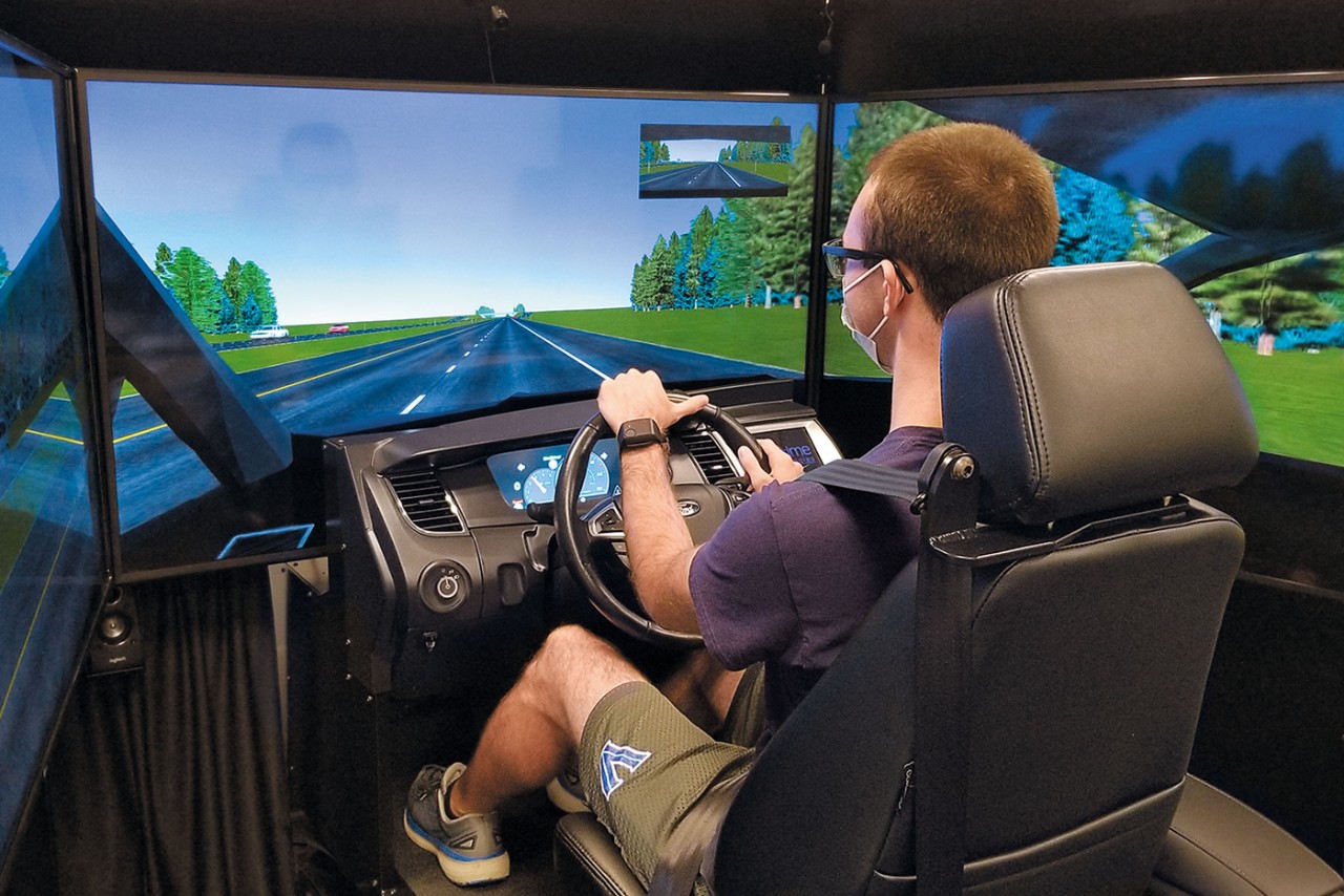 Engineering student on a virtual road behind the wheel of a driving simulator