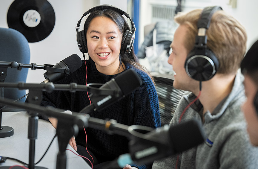 Nursing students wear headsets and sit in front of microphones in the WXVU studio