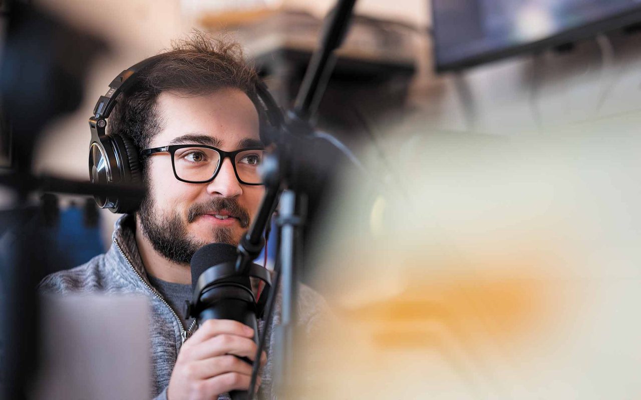 a male radio DJ wears a headset and speaks into the microphone