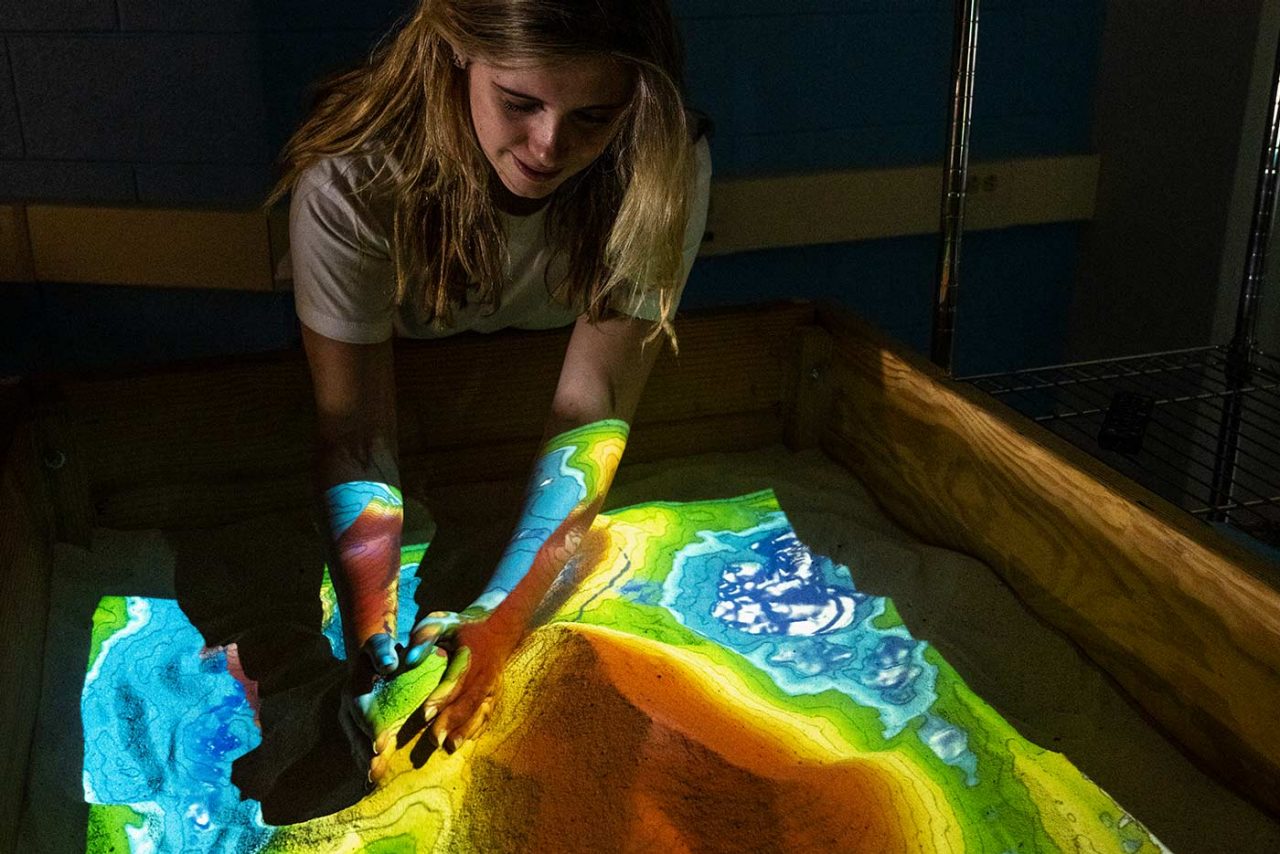 a student uses an augmented reality sandbox to create different geographic formations