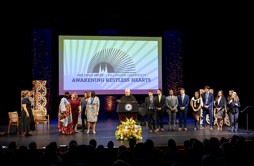 University President the Rev. Peter M. Donohue, OSA, PhD, ’75 CLAS stands at a podium surrounded by Opus Prize finalists and ambassadors