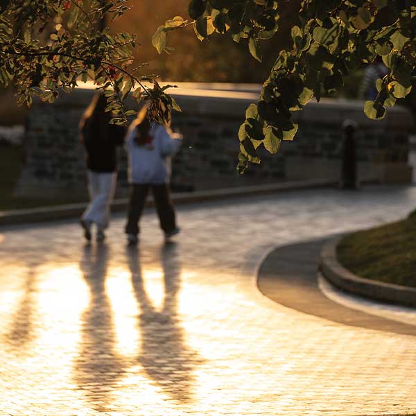 Two students walking along brick pavers on campus.