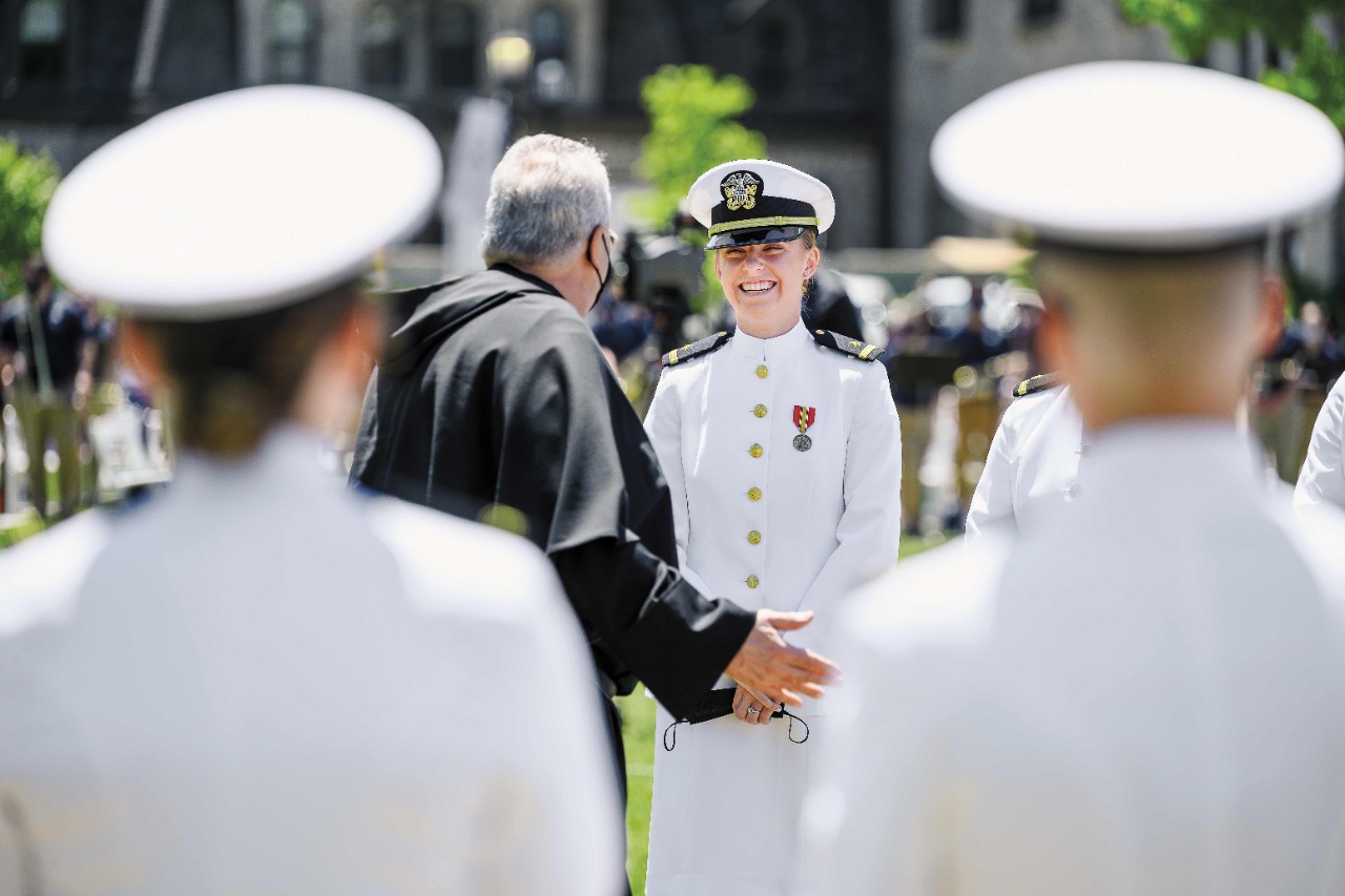 a female member of the NROTC in her white dress Navy uniform smiles at commencement 